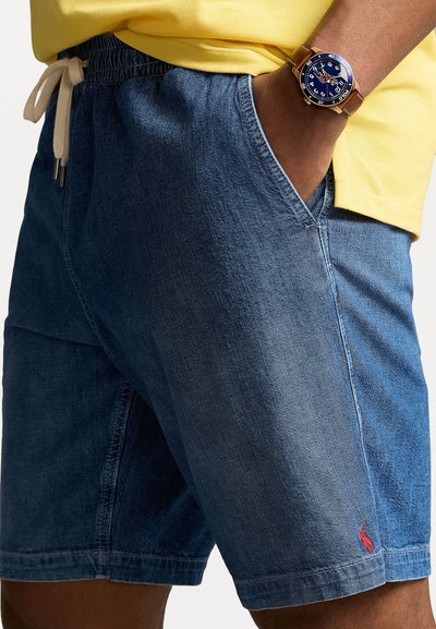 Shorts en denim avec une taille élastique et un cordon de serrage, dotés de poches latérales et d'un petit logo rouge sur l'ourlet gauche.