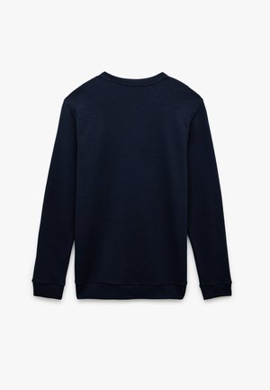 Tummansininen collegepaita, jossa on teksturoitu ribbikuvio, pitkät hihat ja pyöreä pääntie. Takana on yksinkertainen suora helma.