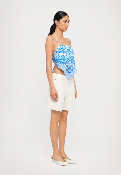 Blue patterned sleeveless top with a square shape, paired with cream-colored shorts. The outfit features delicate straps and a slightly loose fit.