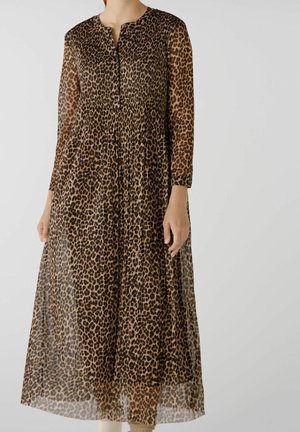 Nainen pukeutuneena pitkähihainen, ruskea leopardikuvioinen midimekko, jossa napit rinnassa ja liehuva hame.