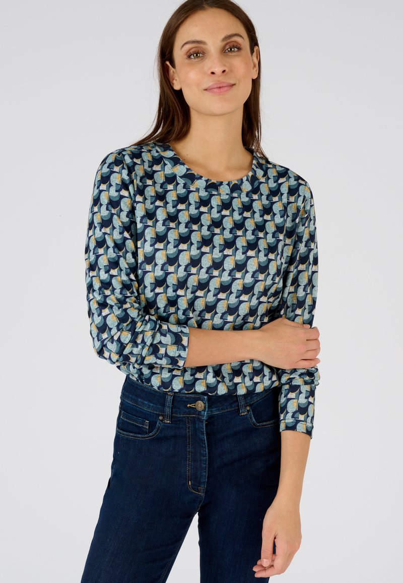 Multikleurige, gepatternde lange mouwen shirt met een ronde halslijn, bedrukt met blauwe, groene en gele vormen. In combinatie met donkerblauwe denim jeans.