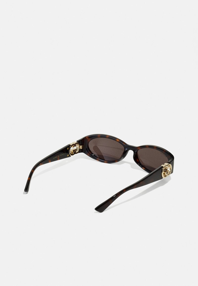 Tortoiseshell sunglasses with oval lenses, dark brown tint, gold hardware accents, and sleek, curved arms. Smooth plastic texture.