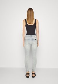 Jeans ajustados de un azul claro con un acabado desgastado y bolsillos traseros, combinados con una camiseta sin mangas negra y sandalias negras, vista desde la parte posterior.