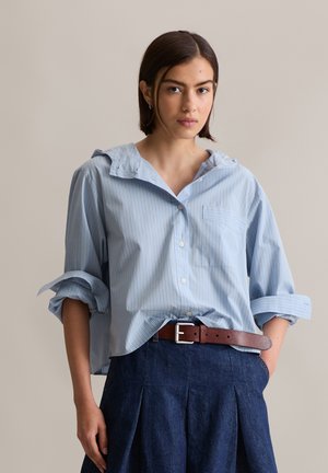 Light blue striped button-up shirt with a large collar and rolled sleeves, paired with a dark denim skirt and brown leather belt.