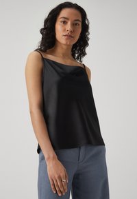 Black satin camisole with a cowl neckline and thin straps, paired with light blue tailored pants. Smooth texture and fluid drape.