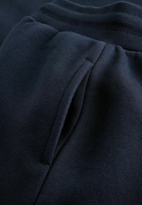 Marineblaue Jogginghose mit strukturiertem Stoff, elastischem Bund und einer seitlichen Tasche, die in das Design integriert ist.