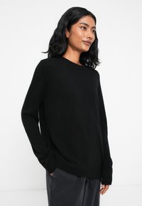 Sweater preto em malha com decote redondo, mangas longas e punhos canelados, apresentando um corte descontraído e uma textura suave.