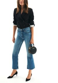 Blazer nero doppiopetto, jeans a vita alta azzurri chiari con leggero svaso, tacchi a punta neri e una piccola borsa nera con dettagli dorati.