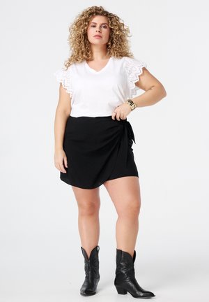 Haut blanc en V avec des manches en dentelle, associé à une mini-jupe noire à nouer. Porte des bottes de cowboy noires. Esthétique simple et épurée.