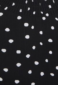 Tessuto nero con pois bianchi irregolari, caratterizzato da una vita elastica arricciata e una superficie liscia e strutturata.