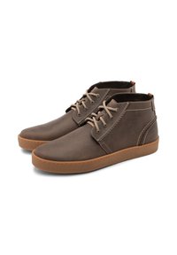 Chaussures montantes en cuir marron avec des lacets beiges, semelles en caoutchouc texturé, coutures contrastées et un petit accent au niveau du talon.