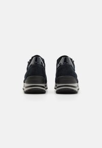Baskets de sport en daim bleu marine avec des accents noirs brillants, dotées d'une semelle superposée avec des rayures grises et noires, conçues pour le confort et la stabilité.