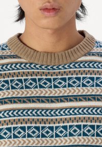 Suéter de punto con cuello acanalado marrón, patrones geométricos en azul verdoso, beige y crema, con una textura suave y grosor medio.