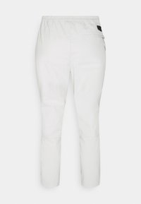 Pantalon blanc à taille élastique avec une poche zippée à l'arrière et un petit écusson de marque noir sur le côté droit près de la taille.