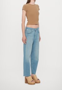 Hnědý žebrovaný top s krátkými rukávy, světle modré džíny se rovnými nohavicemi a béžové platformové sandály s dřevěným podpatkem a cvočky. Jednobarevné bílé pozadí.