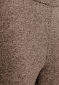 Pantalones de chándal de punto marrones con una textura suave y cinturilla elástica. La imagen de cerca muestra costuras uniformes y una superficie lisa.