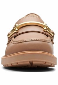 Mocassin en cuir caramel avec semelle à gros crampons et détail en barre métallique dorée sur le dessus, vu de face.
