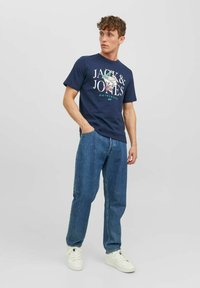 Camiseta de algodón azul marino con un estampado gráfico que dice "JACK & JONES ORIGINALS" y jeans de mezclilla combinados con zapatillas deportivas blancas.