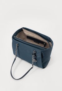 Borsa a spalla in blu navy con un esterno in nylon liscio e manici in pelle. Presenta dettagli in catena color argento e un interno trapuntato beige. Chiusura a zip.