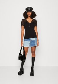 Schwarzes kurzärmliges Oberteil mit Spitzenbesatz und Reißverschlussdetails, kombiniert mit einem Jeans-Minirock. Die Accessoires umfassen eine schwarze Tasche und kniehohe Stiefel.
