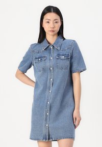 Denim ingruha hegyes gallérral, rövid ujjakkal, két mellzsebbel és elöl gombos záródással. Világoskék színű, puha tapintású.