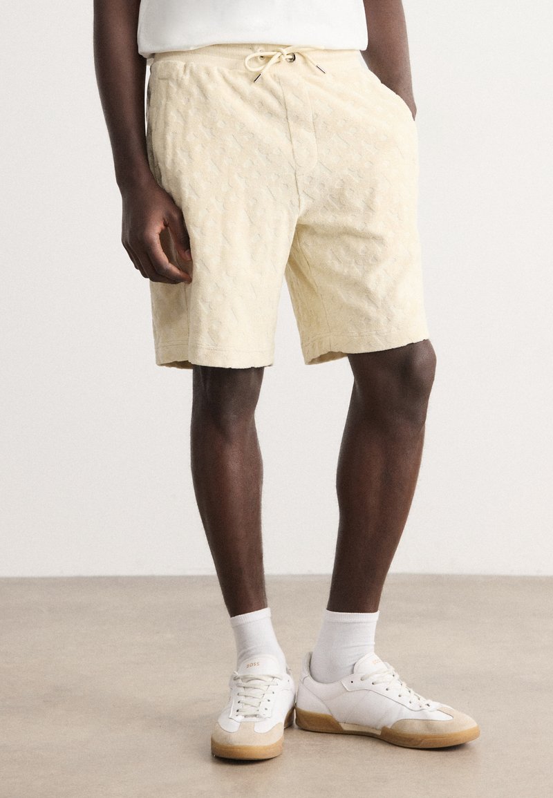 Light yellow shorts with textured pattern, drawstring waist, and side pockets, paired with white sneakers and crew socks.
