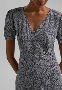 Schwarzes Kleid mit weißem Blumenmuster, kurzen Puffärmeln, tiefem V-Ausschnitt, tailliertem Oberteil und gerafften Details an der Taille.