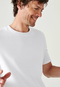T-shirt bianca in cotone con colletto rotondo classico, maniche corte e una texture liscia, caratterizzata da dettagli di cucitura sottili.