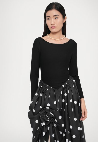 Must pikkade varrukatega pluus paadi-kaelusega, millele on kombineeritud lilledetailidega täpiline seelik, valmistatud siledast kangast.