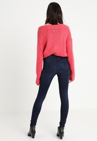 Suéter de punto rosa con mangas anchas, combinado con jeans ajustados de color azul oscuro. Botines negros completan el conjunto.