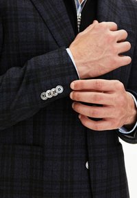 Mörk rutig kavaj med en texturerad tyg, fyra silverknappar vid manschetten och en kontrasterande ljusblå innerfoder.