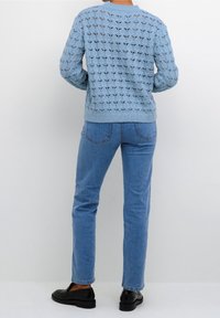 Lichtblauwe gebreide trui met opengewerkte patroon, ronde hals en ribgebreide manchetten, gecombineerd met lichtblauwe denim jeans en zwarte instappers.