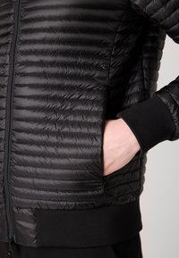 Melna pūkainā jaka ar kvadrātveida rakstu, ar rāvējslēdzēju un ribotām piedurknēm. Gluda tekstūra un pieguļoša forma.