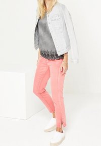 Chaqueta de mezclilla gris claro sobre una blusa de cuadros blanco y negro con dobladillo festoneado, combinada con pantalones rosa brillante y zapatillas blancas sin cordones.