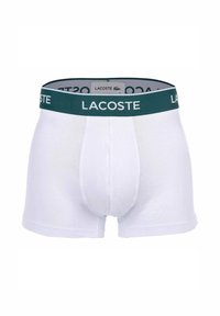 Boxer briefs in cotone bianco con un elastico verde in vita che mostra il logo Lacoste. Texture liscia, design aderente e senza motivi visibili.