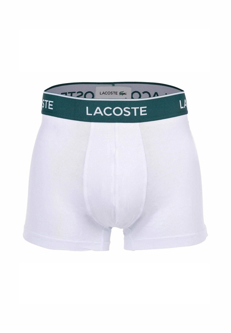 Boxer-briefs en coton blanc avec une taille élastique verte arborant le logo Lacoste. Texture lisse, design ajusté et sans motifs visibles.