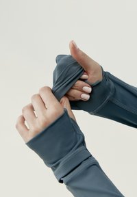 Top ajustado de manga larga en tela azul oscuro, con agujeros para los pulgares y detalles de costura distintivos. Textura suave con un ajuste flexible.