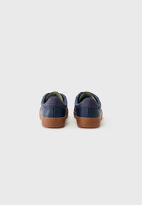Mørkeblå lærersneakers med en teksturert brun gummisåle, som har et lilla hælaksent og grønn innvendig fôring.