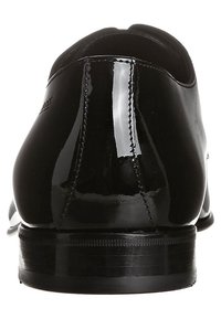 Chaussure habillée en cuir verni noir avec un bout arrondi, une silhouette épurée et des détails de couture minimaux. Texture lisse et brillante. Talon bas.