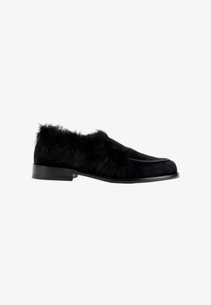 Chaussure loafer noire avec une semelle plate et une fourrure duveteuse couvrant les côtés supérieurs et la zone du talon.