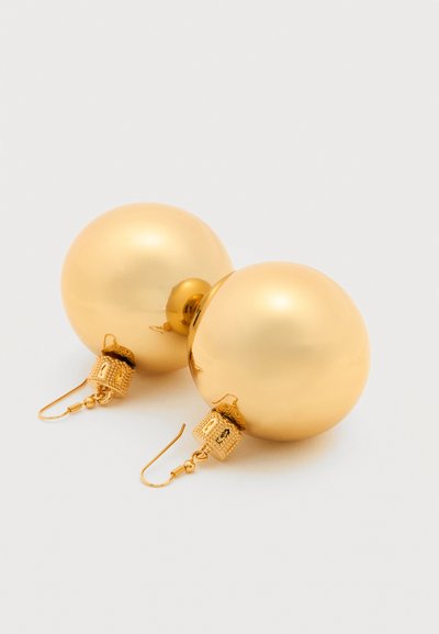 Ζευγάρι μεγάλων, λαμπερών χρυσών σφαιρικών σκουλαρικιών με περίπλοκα υφασμένα αγκίστρια σε απλό φωτεινό φόντο.