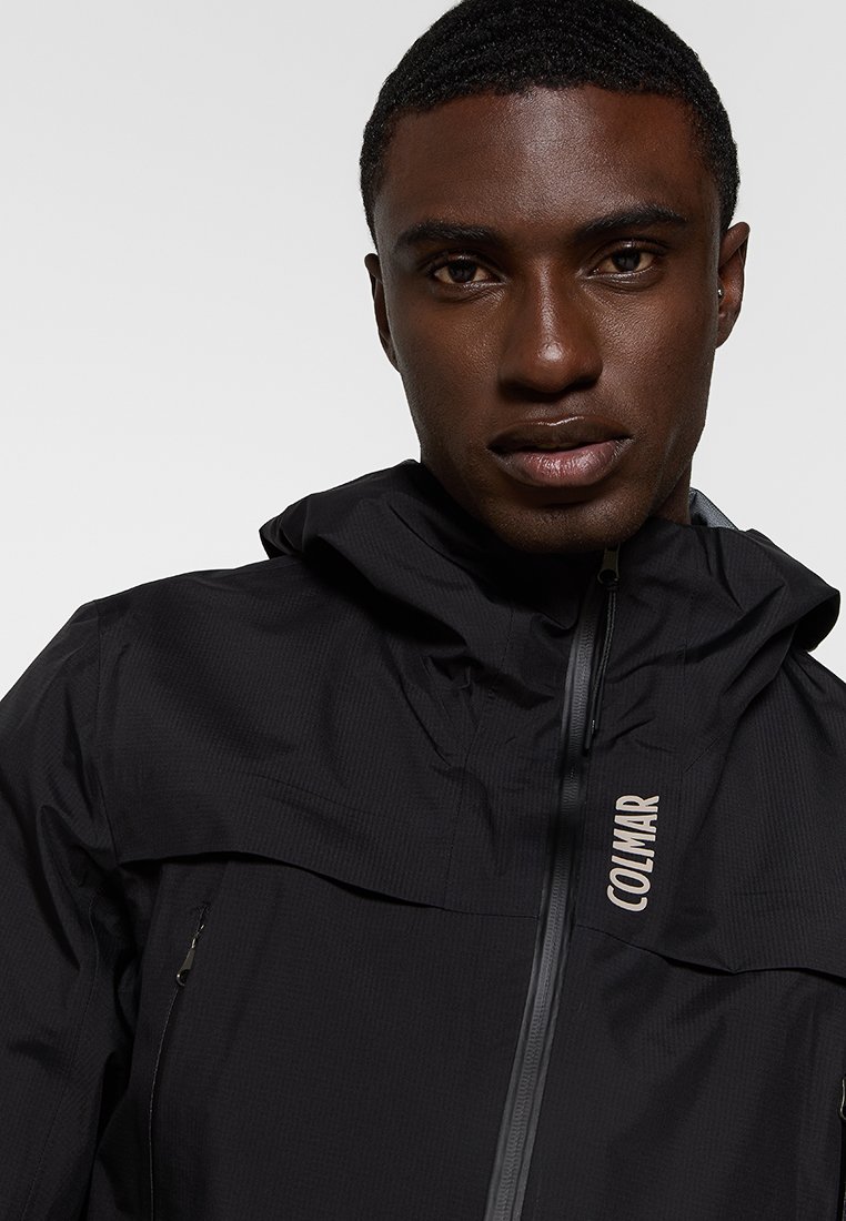 Giacca nera con cappuccio realizzata in tessuto leggero con una sottile trama. Presenta una zip frontale, tasche laterali e un logo sul petto.