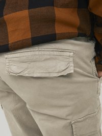 Beige cargo pants with a textured finish; features a flap pocket with visible stitching, paired with a brown and black plaid shirt.