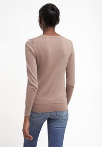 Beige åtsittande tröja med rund halsringning och långa ärmar, tillverkad av ett mjukt stickat tyg. Kombinerad med blå denimjeans.