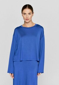 Blå løs pasform langærmet top i blødt, glat stof med rund halsudskæring og sænkede skuldre, båret over en matchende kjole.