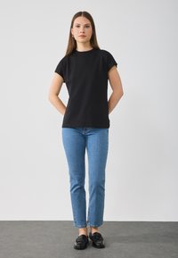 Zwarte katoenen T-shirt met korte mouwen, gecombineerd met lichtblauwe rechte spijkerbroeken en zwarte instappers. Eenvoudige, klassieke ontwerpdetails.