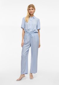 Gaiši zils, īsām piedurknēm, pogājams krekls ar apkakli, apvienots ar brīviem, elastīgas jostas biksēm. Raksturo zīda struktūra un plašs kāju griezums.