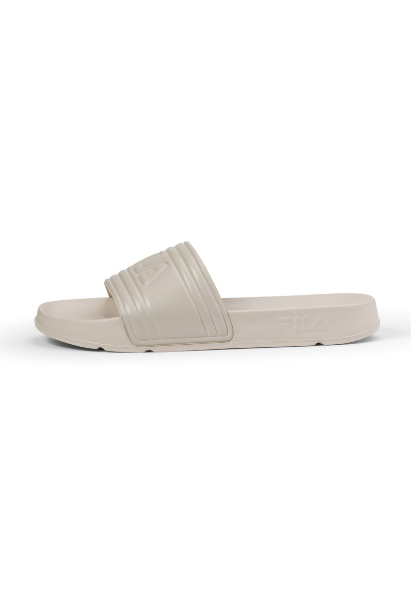 Beige gummiskor med bred rem som har en räfflad design och logo, platt sula och slät yta. Lämpliga för avslappnad användning.