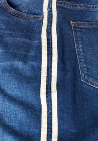 Tejido de mezclilla en azul con una raya blanca vertical. Cuenta con un bolsillo trasero y detalles de costura visibles. La textura parece suave y ligeramente desgastada.
