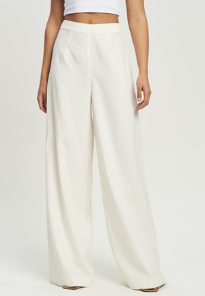 Pantalons larges blancs à taille haute, en tissu lisse. Présente des poches latérales et un design épuré et ajusté.